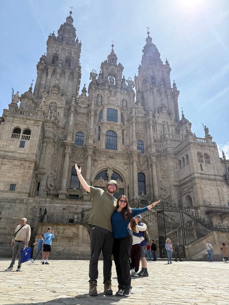 Two students posing in front of the Santiago de Compostela Cathedral in Spain on a sunny, spring day.
