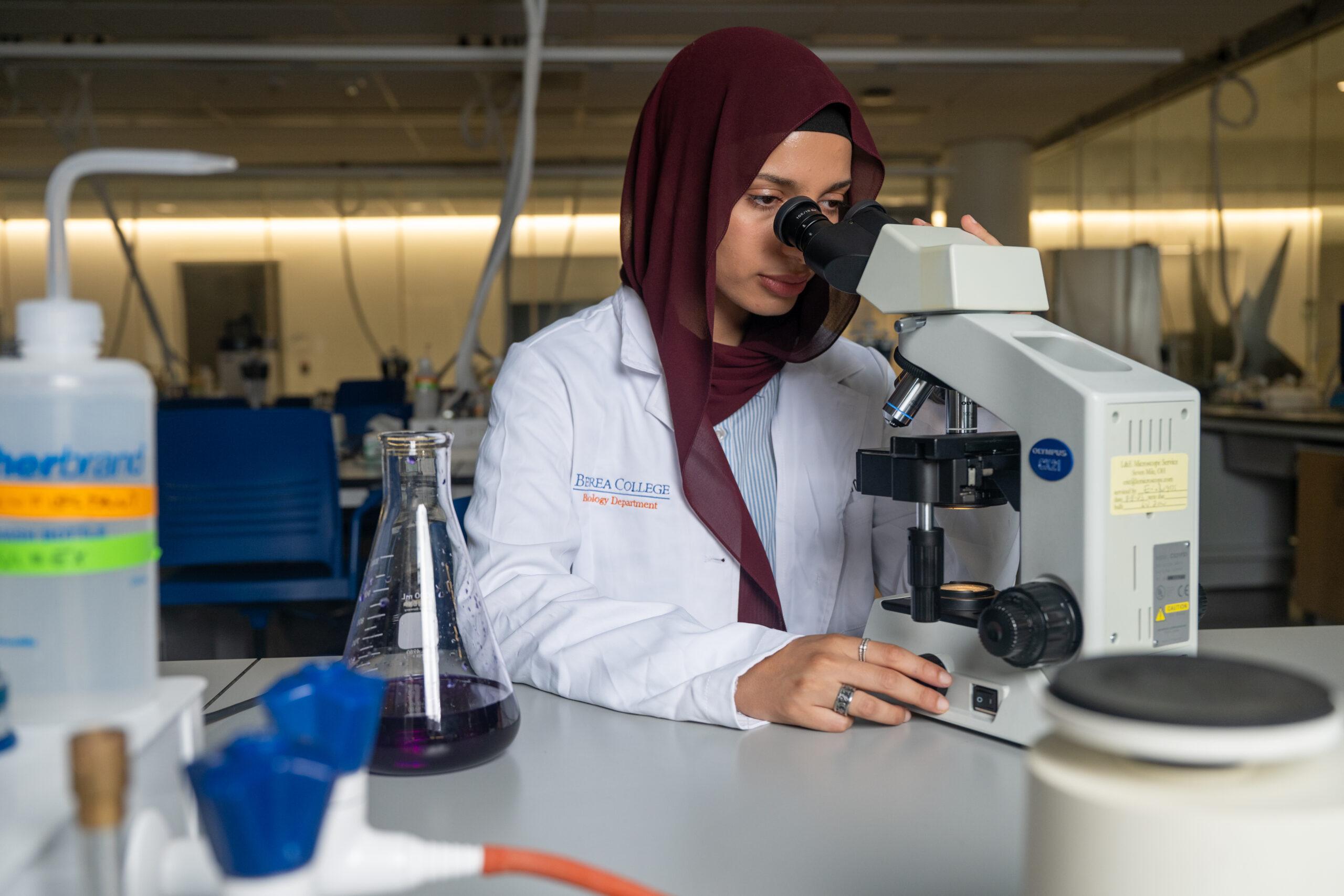 A Berea College student is looking though a microscope in a science laboratory.